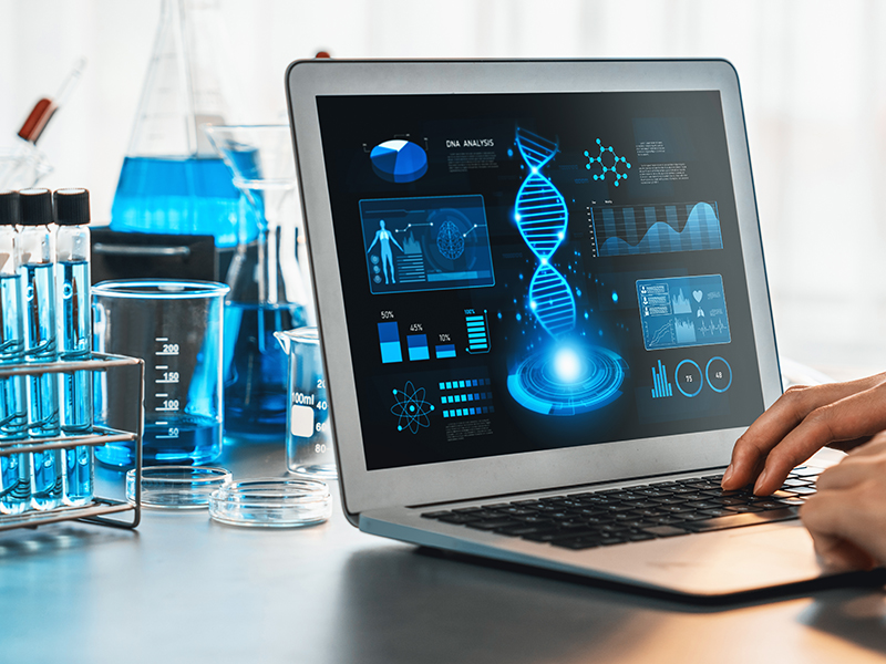 Photograph of biomedical lab setting. A laptop displays various health data and graphs. 