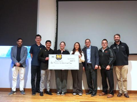 Students at University of Northern Colorado stand on stage with a large check won during a NASA Tech Transfer University pitch event