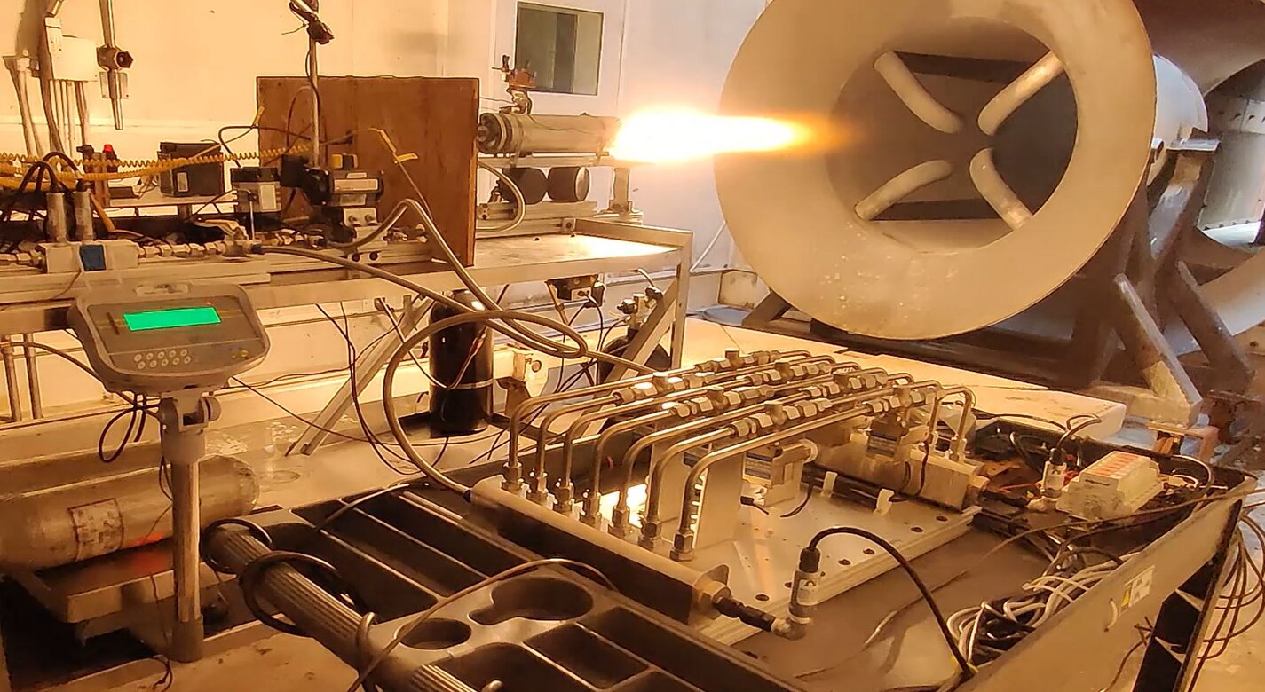 Image of the hot-fire test of the fast-acting, deep-throttling hybrid motor at Utah State Universitys Propulsion Research Laboratory. The digital valve is shown in the foreground, and the hybrid motor is in the background of the frame.