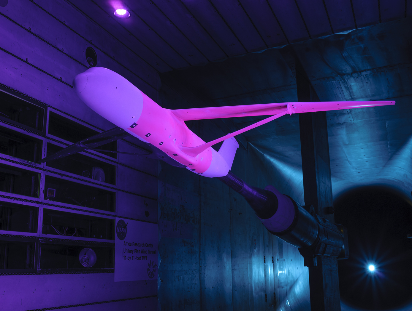 An aircraft design that could reduce fuel use, emissions and noise is set up for a test in a wind tunnel at NASA's Ames Research Center in California in which pink-colored pressure-sensitive paint is applied to the vehicle. The pink paint shines when exposed to blue light, glowing brighter or dimmer depending on air pressure in the area.